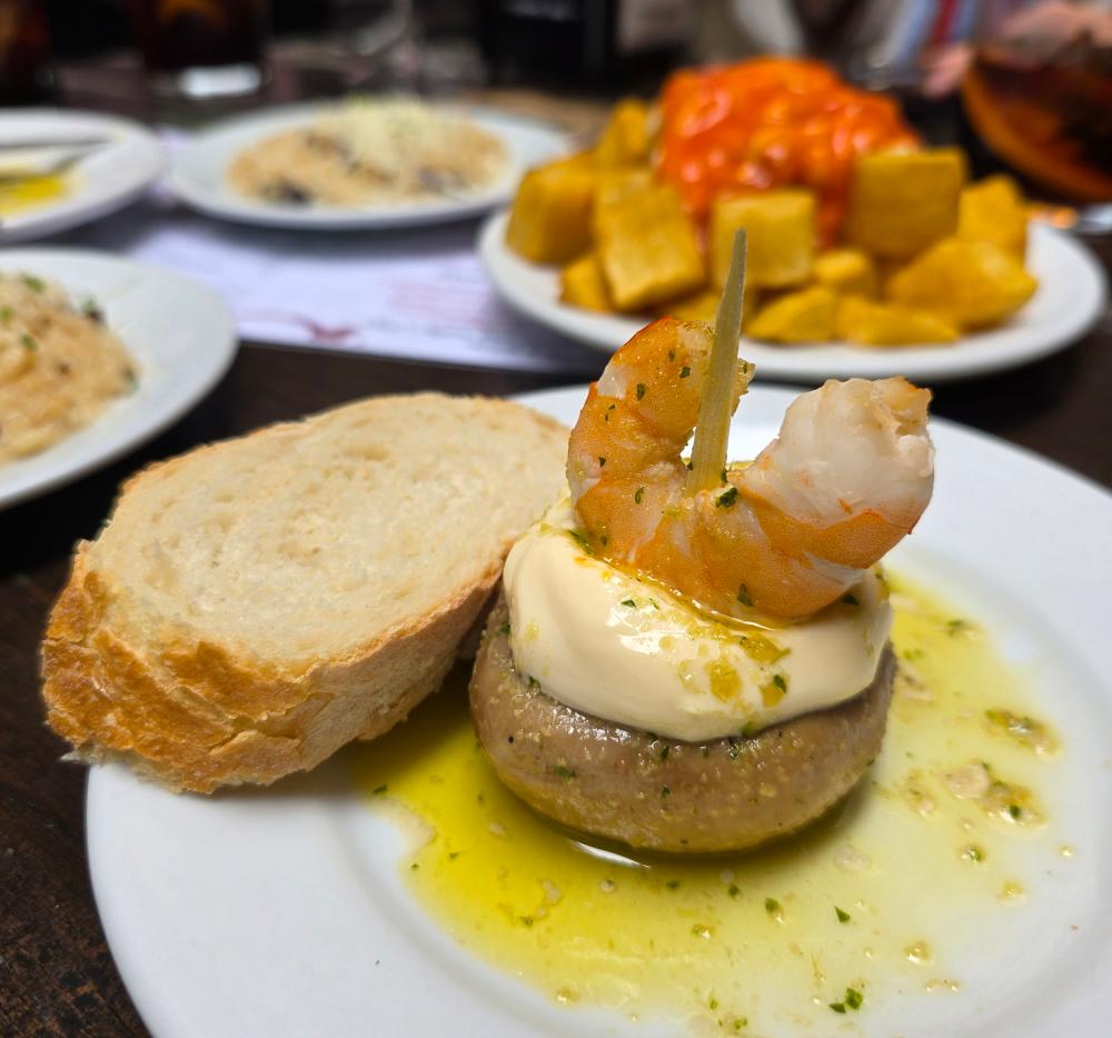 pincho de champiñón y gamba y detrás plato de patatas bravas